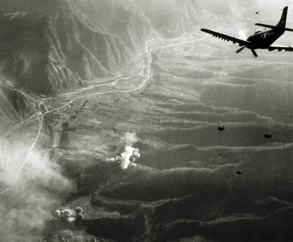 Photo of from the air of a US Skyraider from Attack Squadron 75 dropping three bombs over the Korean countryside during the Korean War, Korea. Smoke rises from bombs that have hit the ground. The planes flew from the US Navy aircraft carrier the USS 'Bon Homme Richard 1952